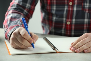 Man writing with pen in notebook at white table, closeup