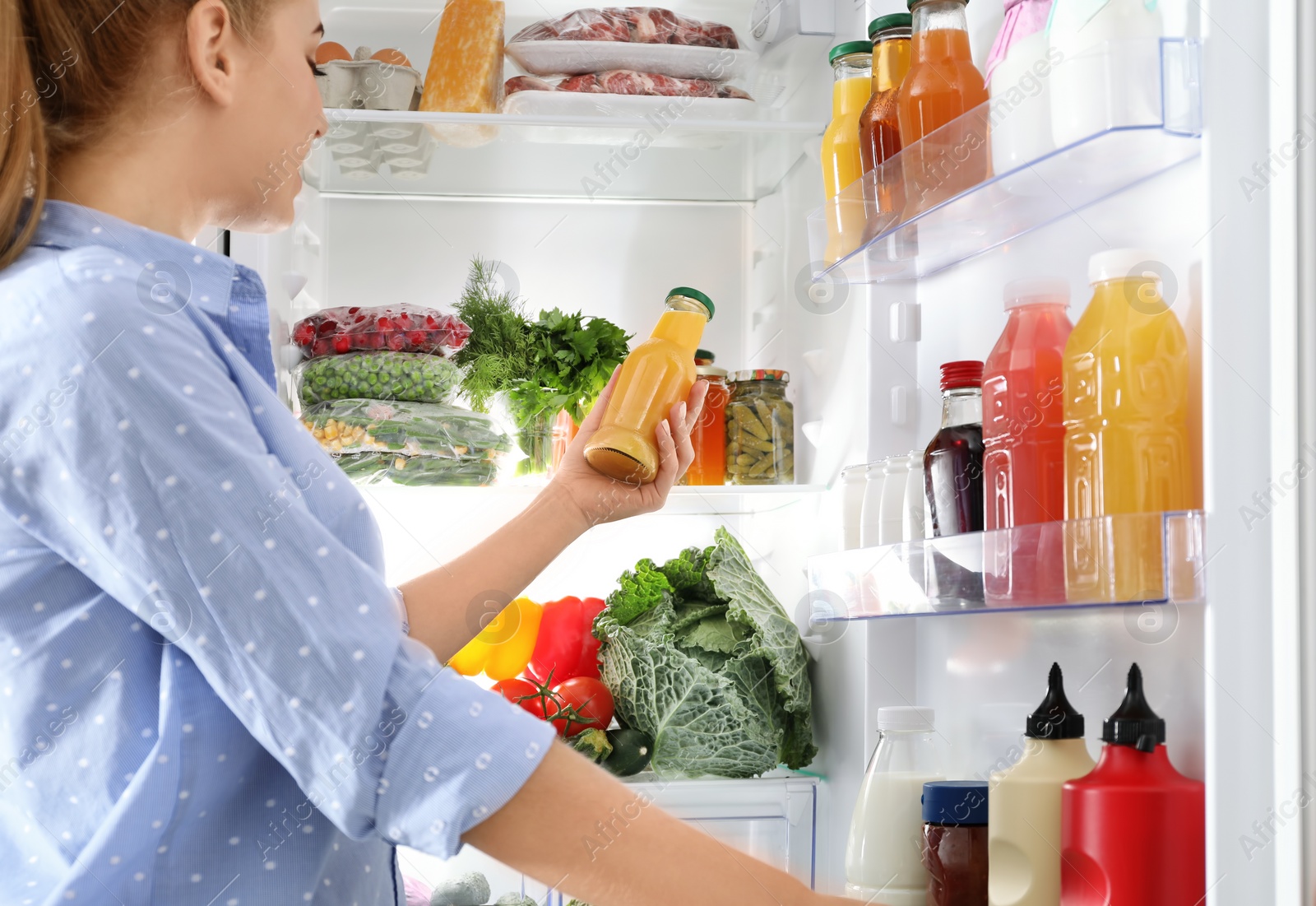 Photo of Woman taking bottle with juice out of refrigerator in kitchen