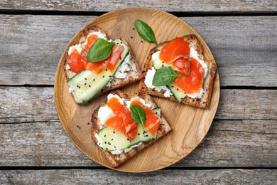 Delicious sandwiches with cream cheese, salmon, cucumber and spinach on wooden table, top view