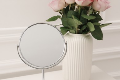 Photo of Mirror and vase with pink roses on white dressing table, closeup