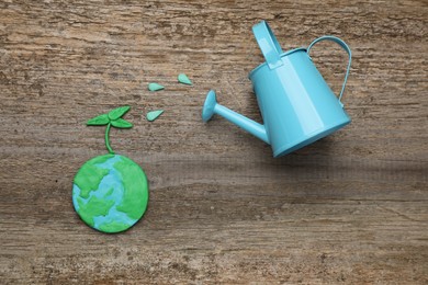 Photo of Happy Earth Day. Flat lay composition with plasticine planet and watering can on wooden table