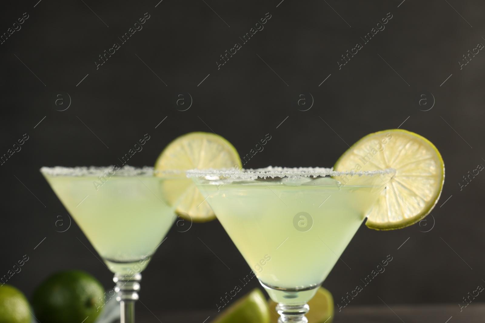 Photo of Delicious Margarita cocktail with salt and lime against blurred background, closeup