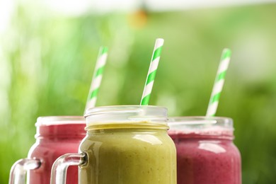 Photo of Different delicious smoothies in mason jars on blurred background, closeup