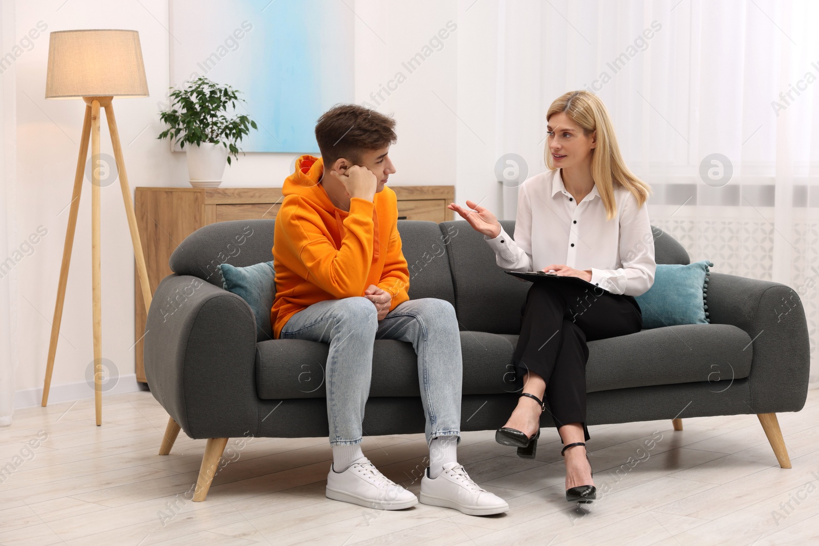 Photo of Psychologist working with teenage boy on sofa in office