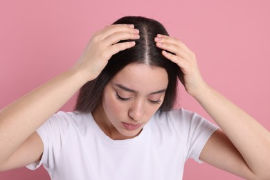 Woman examining her hair and scalp on pink background