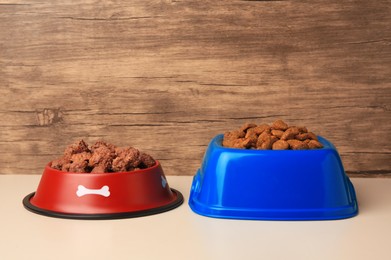 Photo of Dry and wet pet food in feeding bowls on beige background