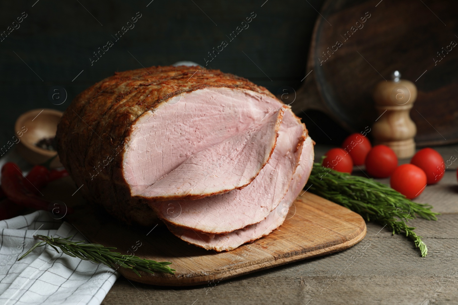 Photo of Delicious baked ham, tomatoes and rosemary on grey wooden table