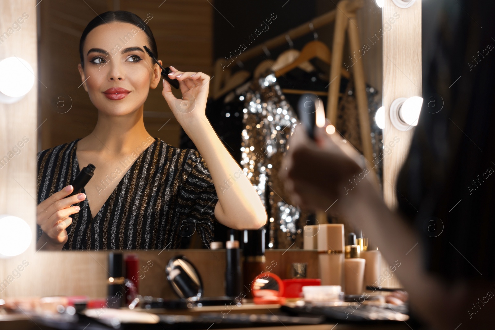 Photo of Bright makeup. Beautiful woman applying mascara near mirror in dressing room