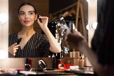 Bright makeup. Beautiful woman applying mascara near mirror in dressing room