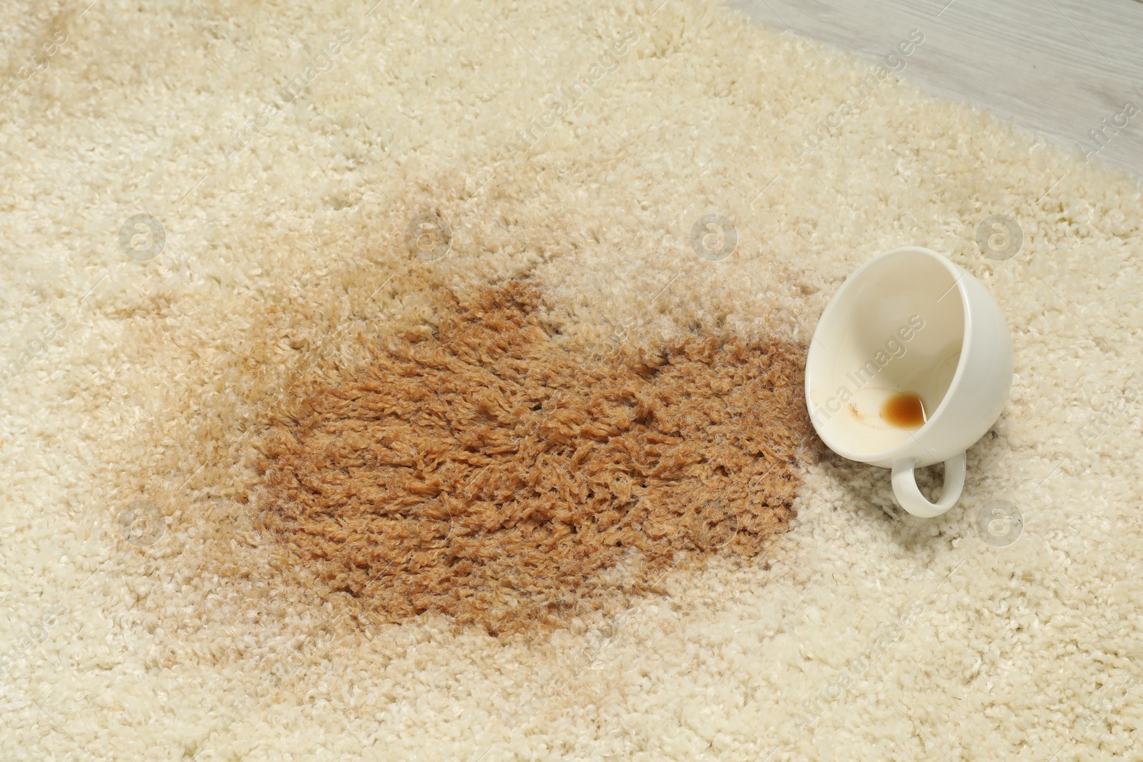 Photo of Overturned cup and spilled coffee on beige carpet, closeup