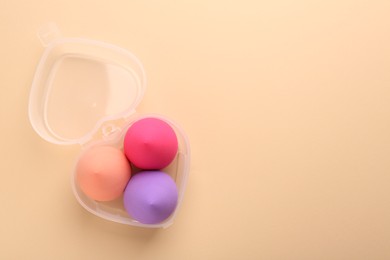 Photo of Many different makeup sponges in plastic container on beige background, top view. Space for text