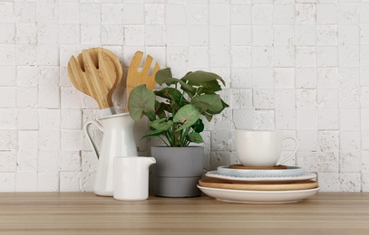 Photo of Green plant and different kitchenware on table near brick wall. Modern interior design