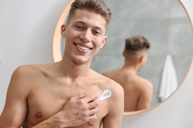Photo of Handsome man applying moisturizing cream onto his shoulder indoors. Space for text