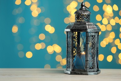 Photo of Traditional Arabic lantern on wooden table against light blue background with blurred lights. Space for text