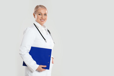 Photo of Mature doctor with clipboard on light grey background. Space for text