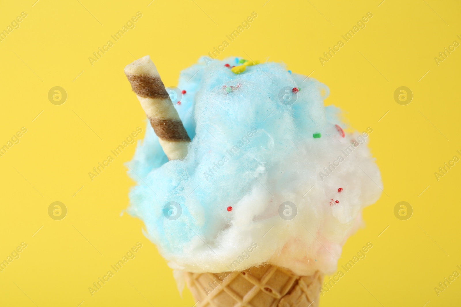 Photo of Sweet cotton candy in waffle cone on yellow background, closeup