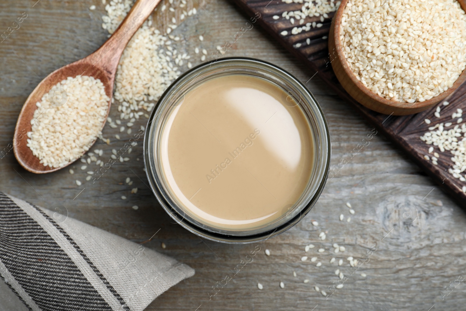 Photo of Jar of tasty sesame paste and seeds on wooden table, flat lay