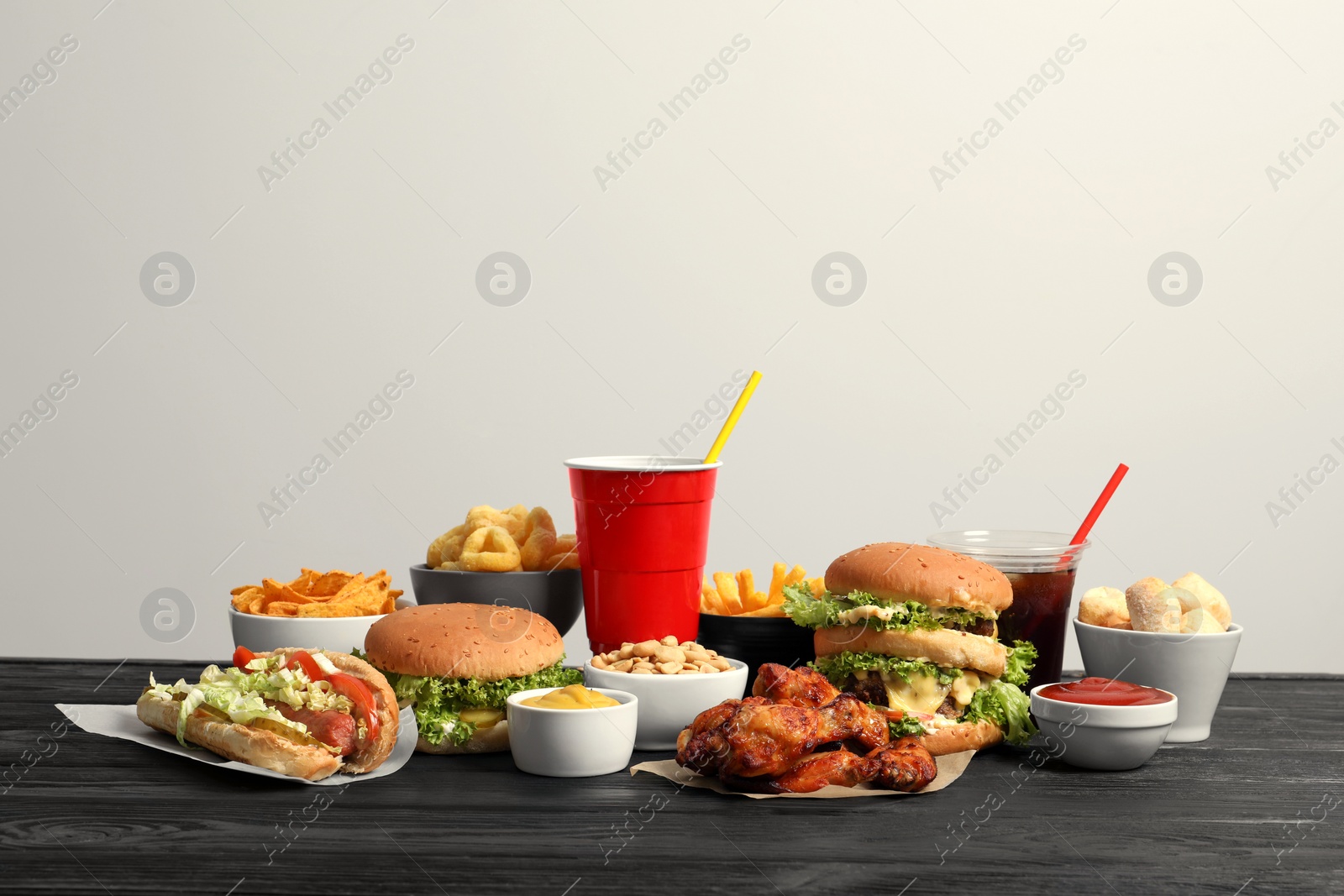 Photo of French fries, burgers and other fast food on wooden table against white background