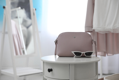 Stylish woman's bag and sunglasses on table in room. Space for text