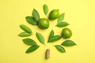 Flat lay composition with fresh green citrus leaves and limes on yellow background