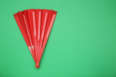 Photo of Bright red hand fan on green background, top view. Space for text