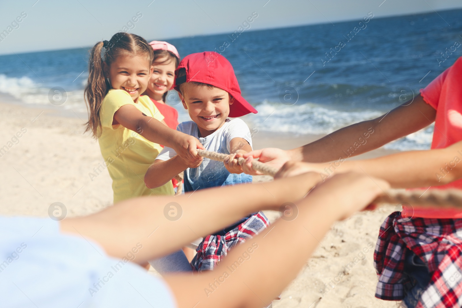 Photo of Cute children pulling rope during tug of war game on beach. Summer camp