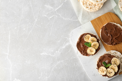 Puffed rice cakes with chocolate spread, banana and mint on grey marble table, flat lay. Space for text