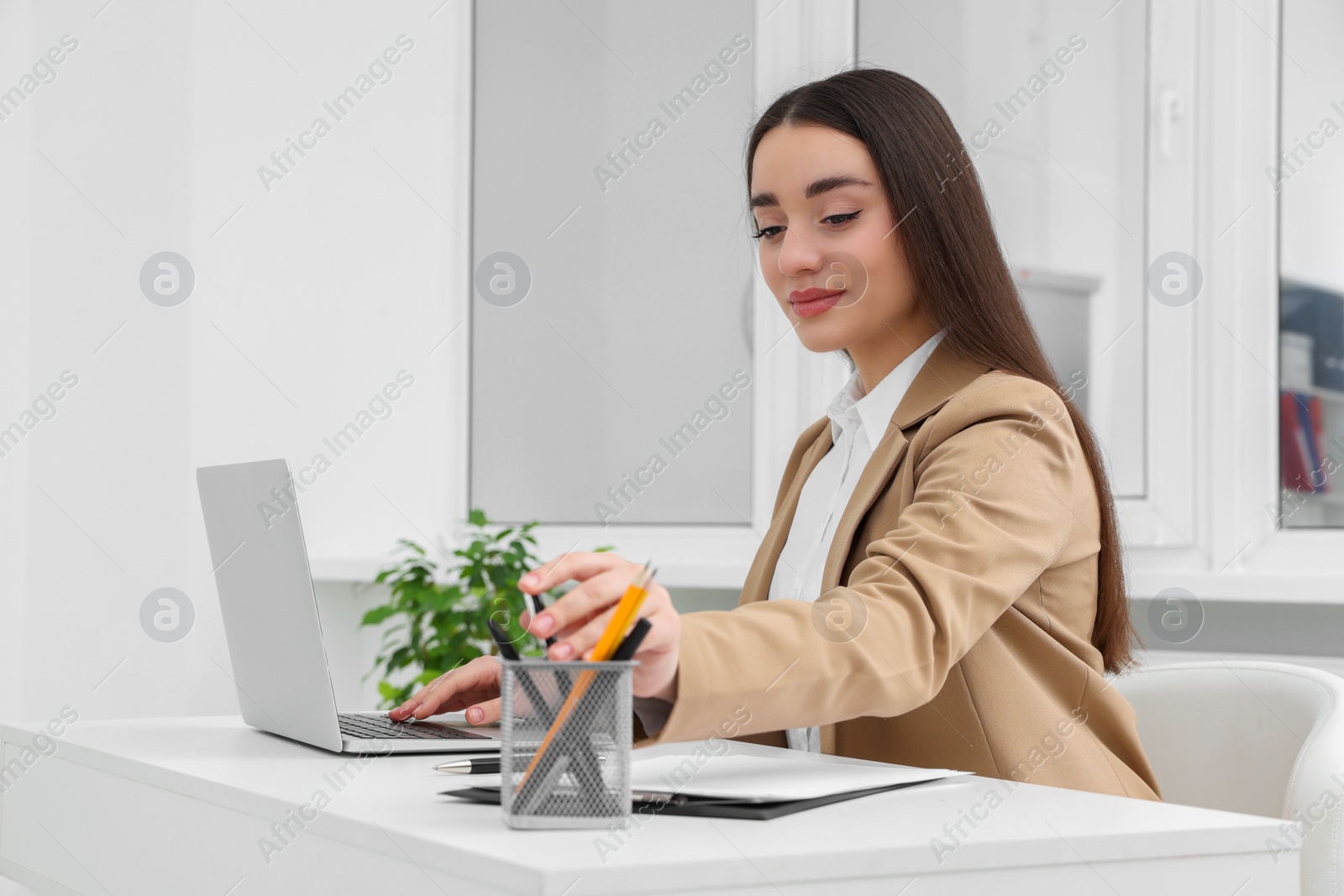 Photo of Young female intern working with laptop at table in office