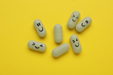 Colorful antidepressants with happy emoticons on yellow background, flat lay