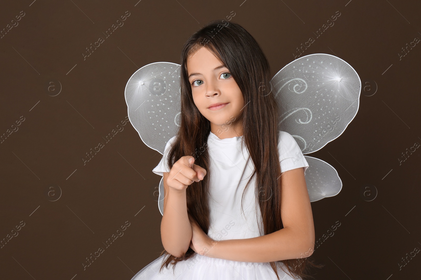 Photo of Cute little girl in fairy costume with white wings on brown background