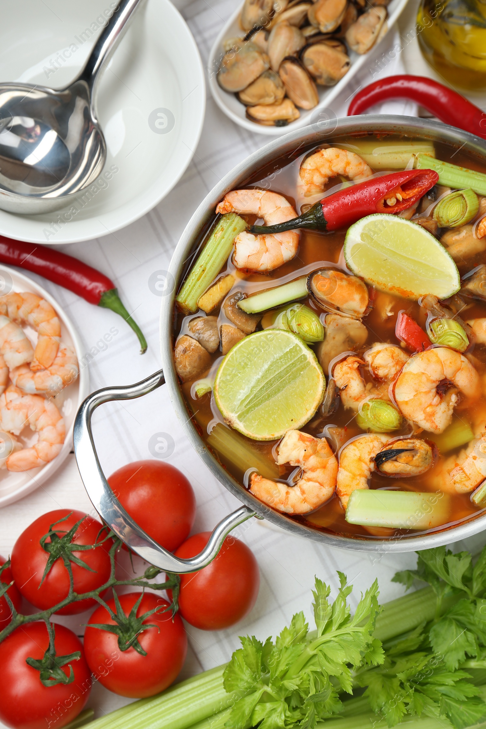 Photo of Saucepan with delicious Tom Yum soup and ingredients on white wooden table, flat lay