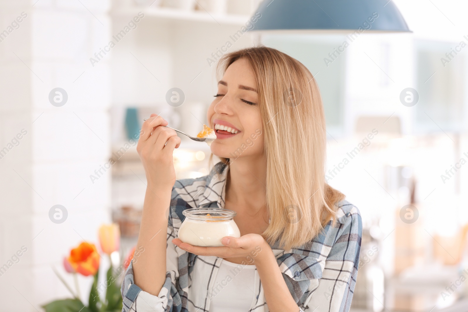 Photo of Young attractive woman eating tasty yogurt in kitchen