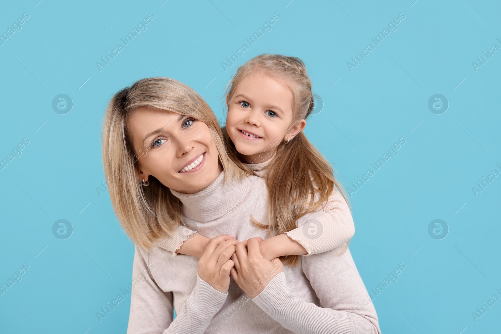 Photo of Daughter hugging her happy mother on light blue background