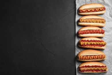 Photo of Fresh delicious hot dogs with sauces on black table, top view. Space for text