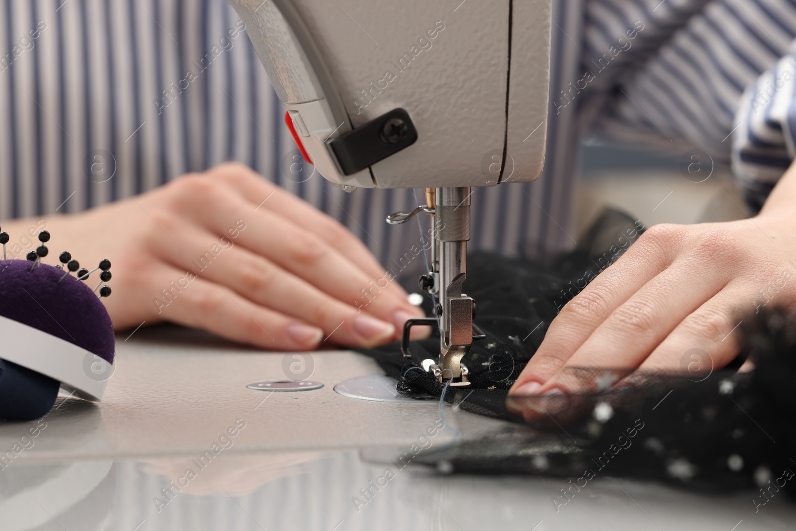 Photo of Dressmaker sewing new dress with machine in atelier, closeup