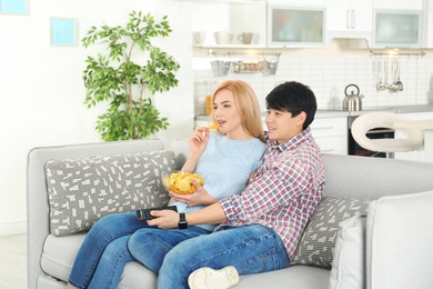 Photo of Young couple with bowl of chips watching TV on sofa at home