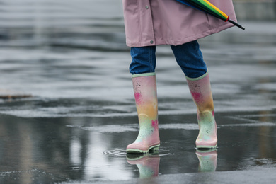 Photo of Woman in rubber boots walking outdoors on rainy day, closeup. Space for text