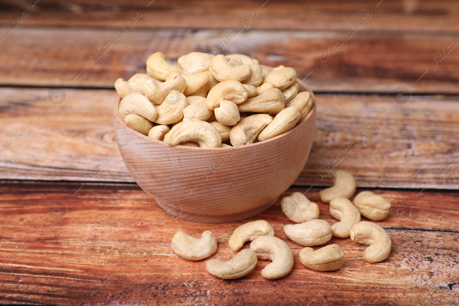 Photo of Tasty cashew nuts in bowl on wooden table