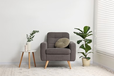 Comfortable armchair, pillow, side table and green houseplants indoors