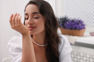 Photo of Beautiful young woman with essential oil on wrist indoors