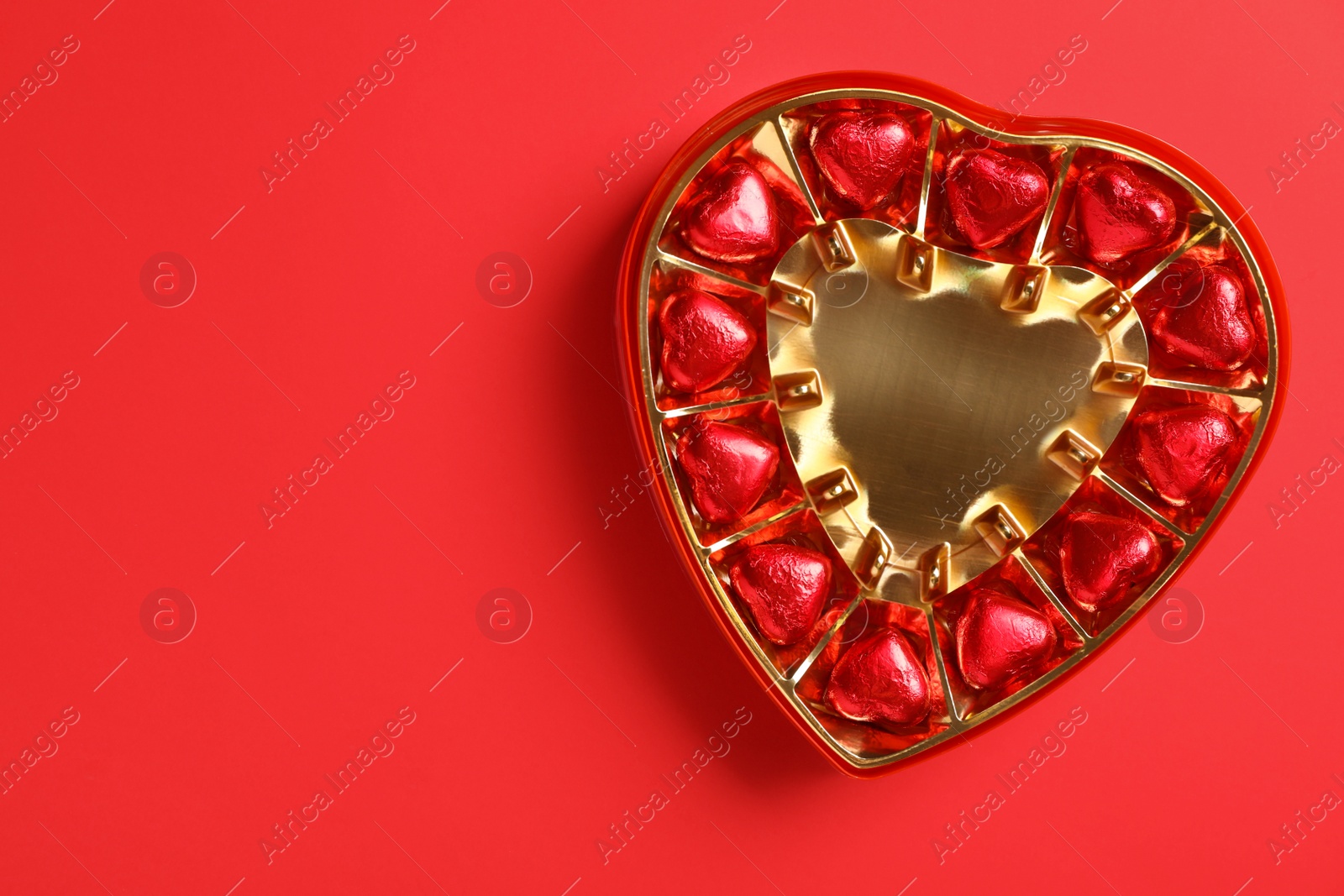 Photo of Tasty chocolate heart shaped candies in box on red background, top view. Space for text