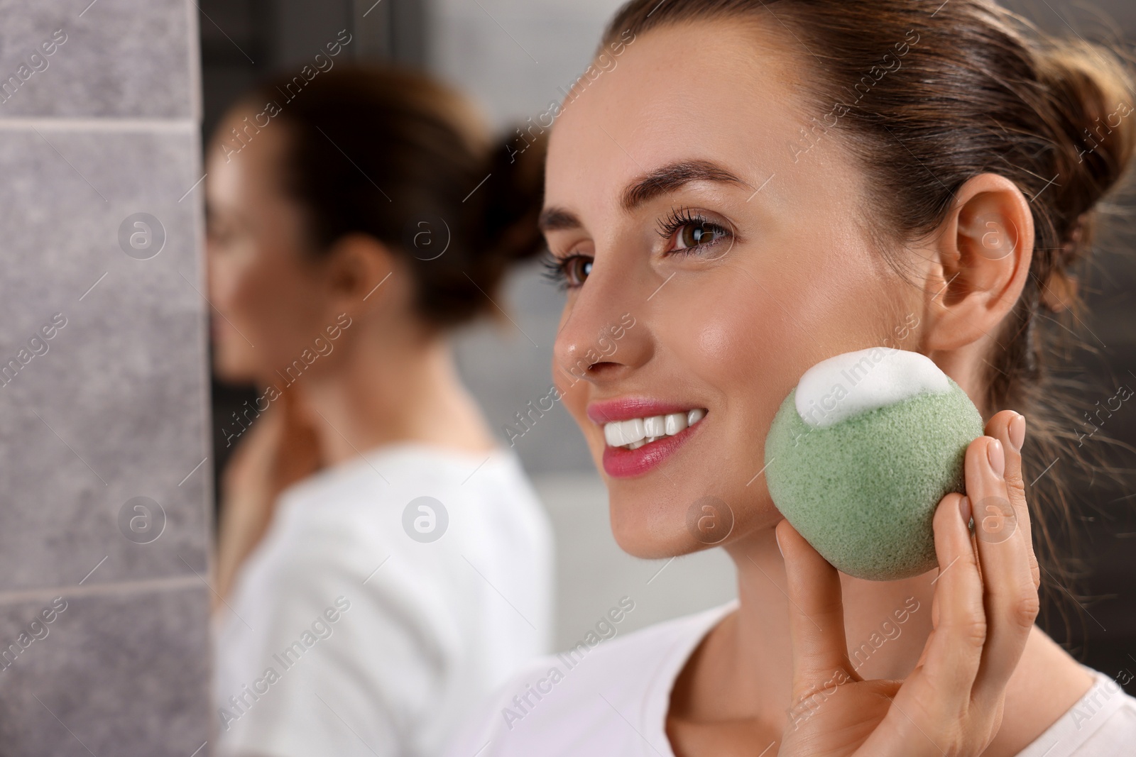 Photo of Happy young woman washing her face with sponge in bathroom. Space for text