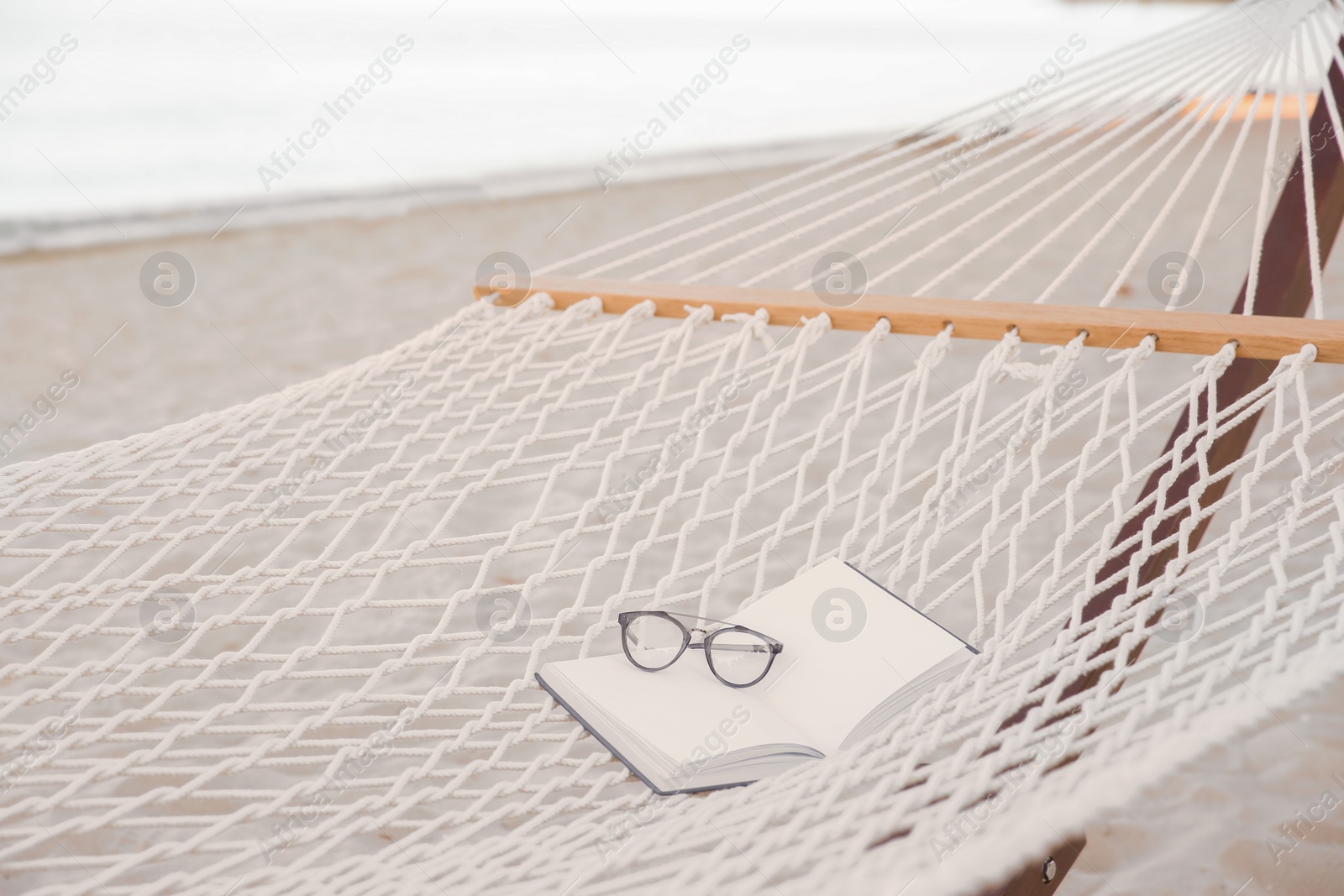 Photo of Comfortable hammock with book and glasses at seaside