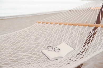 Photo of Comfortable hammock with book and glasses at seaside