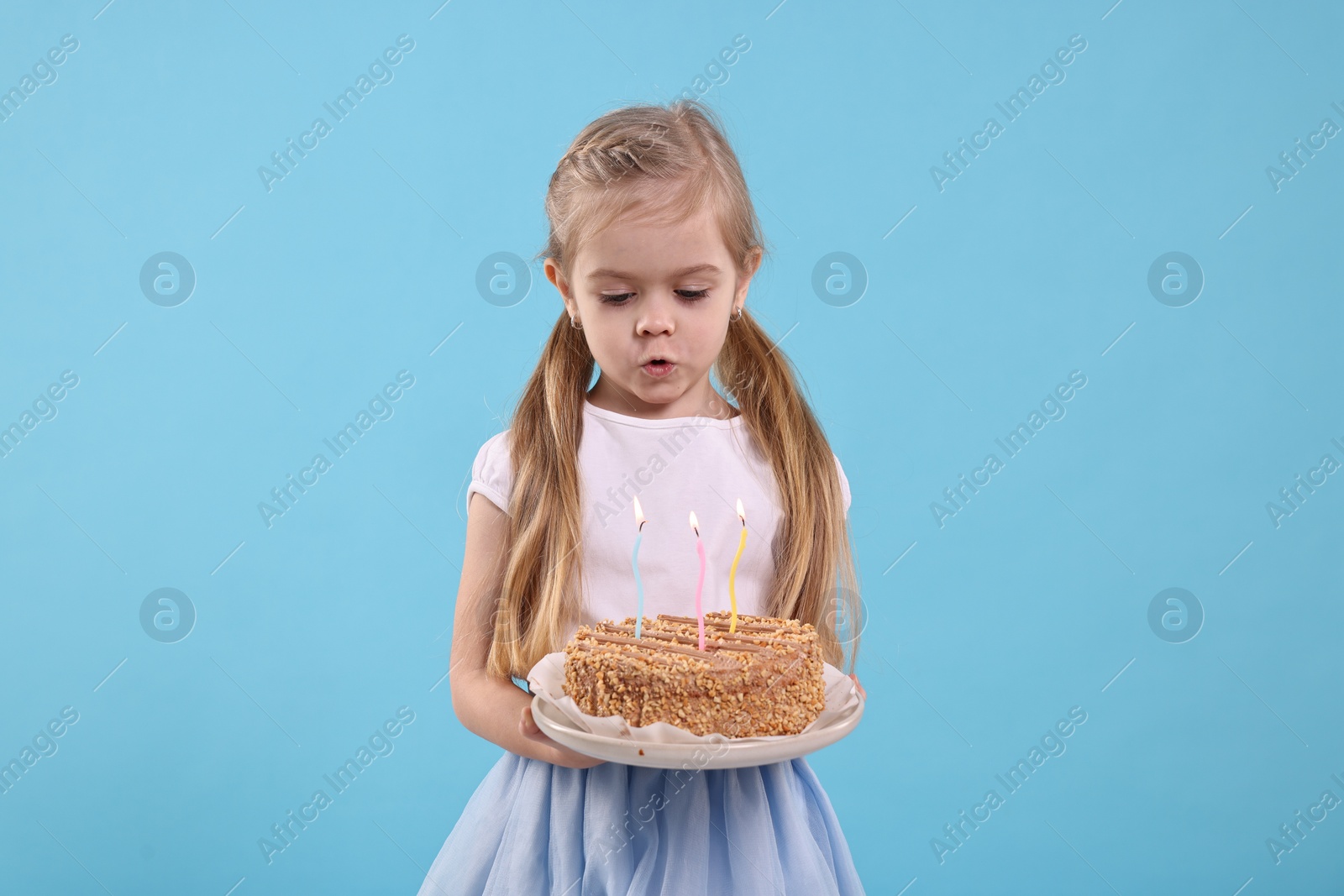 Photo of Birthday celebration. Cute little girl holding tasty cake with burning candles on light blue background