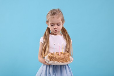 Photo of Birthday celebration. Cute little girl holding tasty cake with burning candles on light blue background