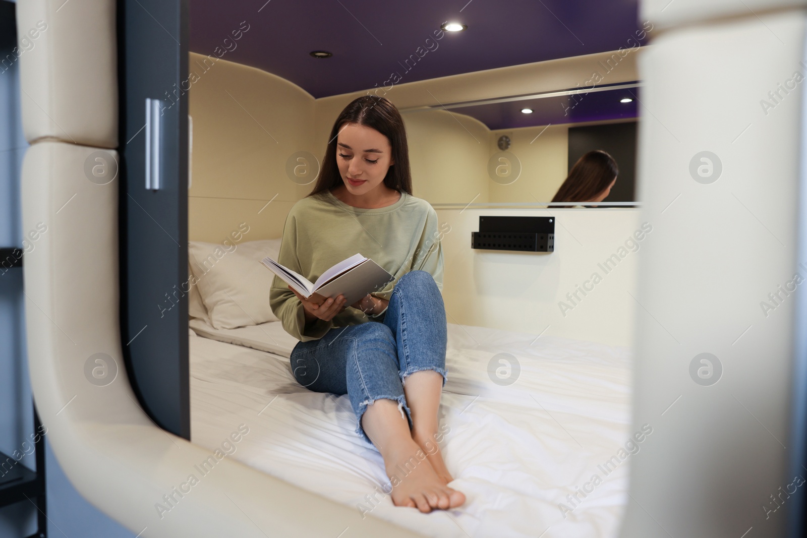 Photo of Young woman reading book in capsule of pod hostel