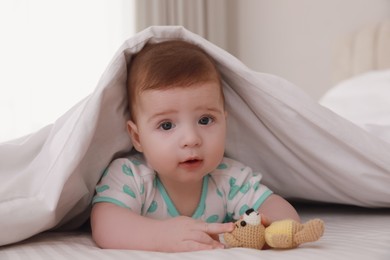 Photo of Cute little baby with toy in bed under soft blanket indoors