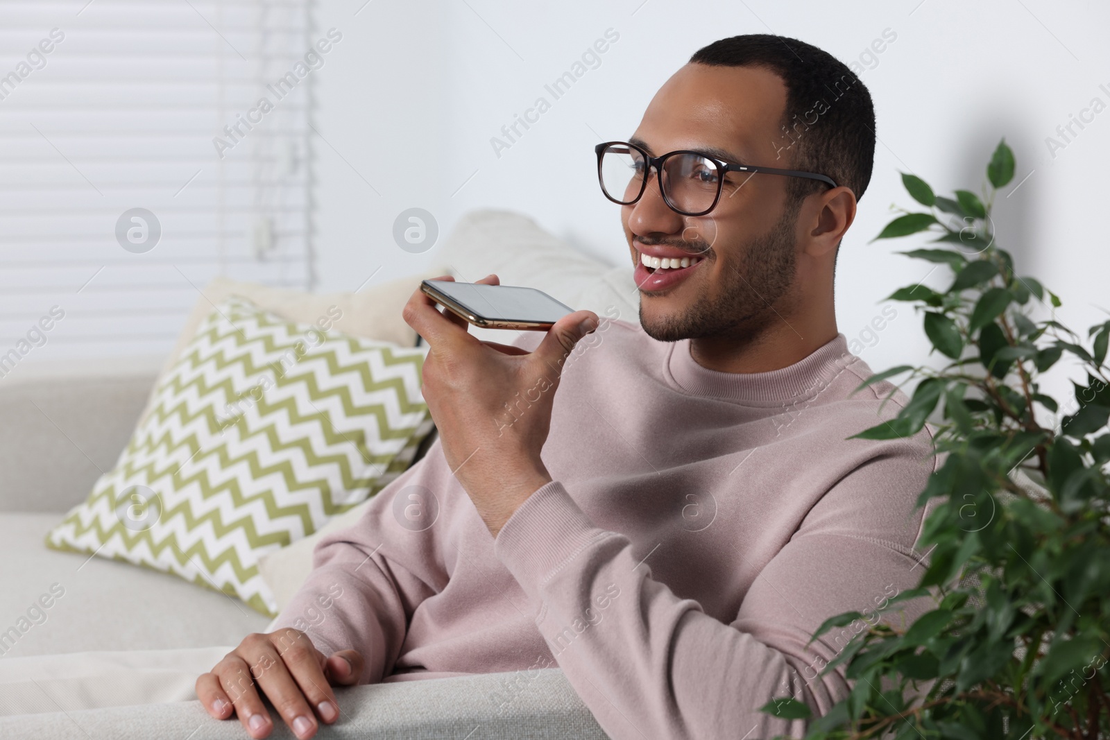 Photo of Happy man sending voice message via smartphone indoors