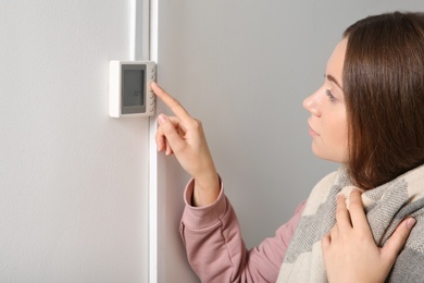 Photo of Woman adjusting thermostat on white wall. Heating system